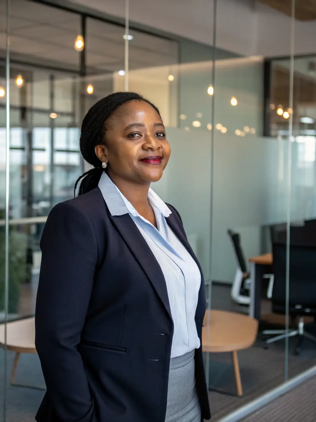 A professional headshot of Ms. Nomusa Dube, a cybersecurity expert, with a serious and focused expression. She is wearing professional attire and standing in a modern office setting.